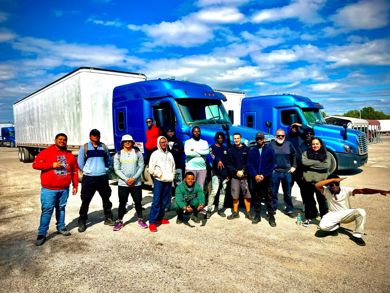 CDL students posing in front of a row of blue tractor-trailers at Tampa Truck Driving School